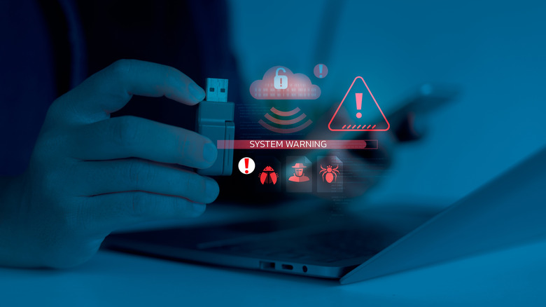 A person holding a USB drive by a laptop