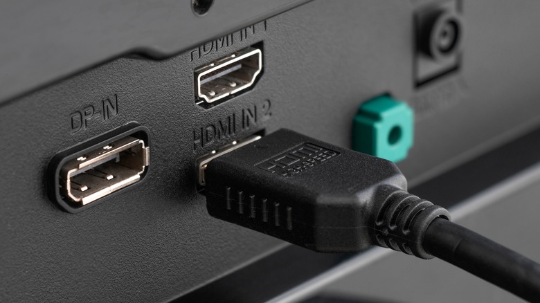 An HDMI cable plugged into the backside of a monitor, showing other unplugged DP and HDMI ports nearby