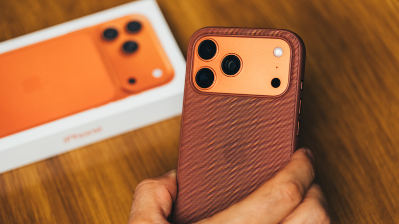 A hand holding an iPhone with a burgundy case, the box in the background.