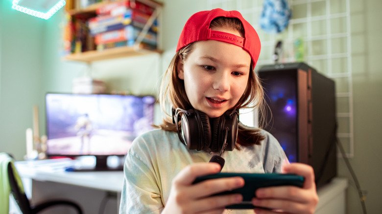 a young woman playing a video game on a phone in her room