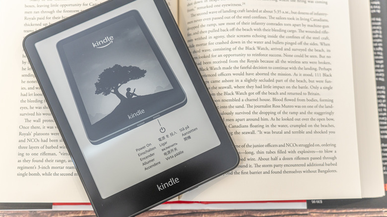 An Amazon Kindle e-reader atop a paperback book.