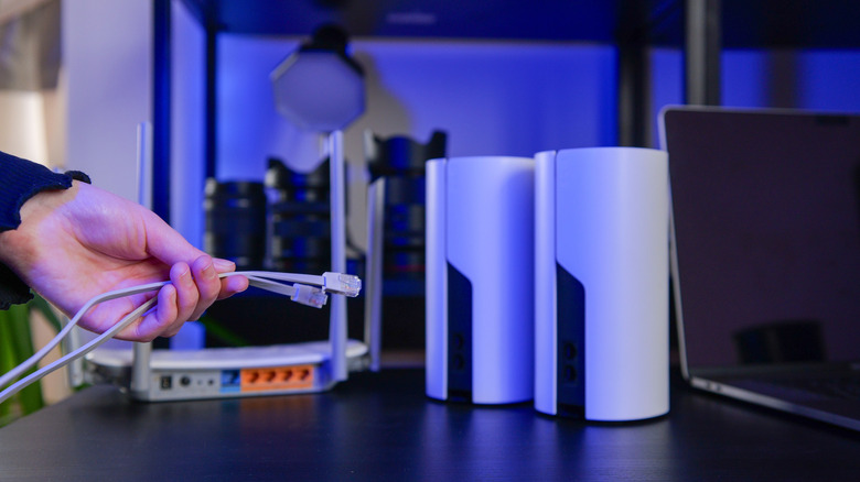 A hand connecting Ethernet cables to a set of Wi-Fi routers.