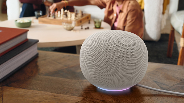 Two people playing chess in the background, a Google Home smart speaker in the foreground.