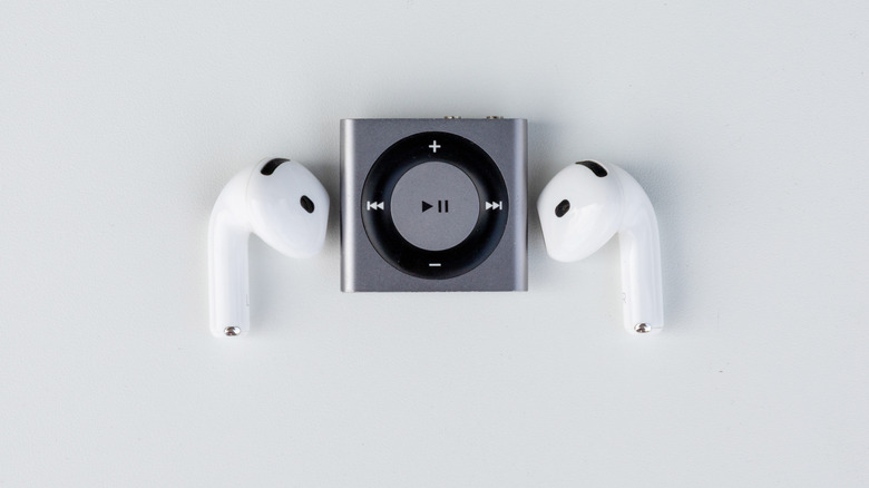 Compact MP3 player placed between two wireless earbuds on white background