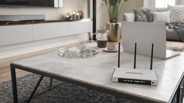 Nondescript internet router on a coffee table next to a laptop.