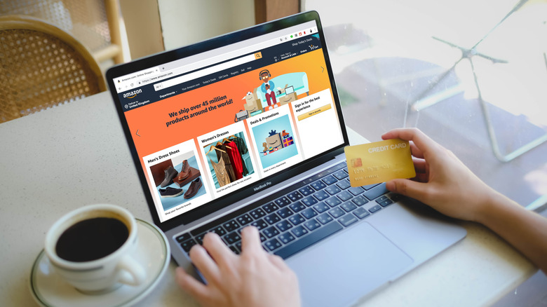 Hands on a laptop visiting the Amazon home page with a credit card in the right hand