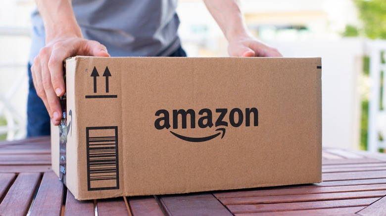 A person in a light blue shirt with both their hands on an Amazon package