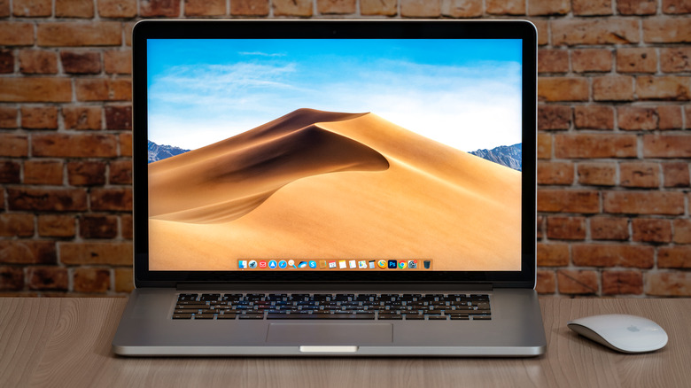 A MacBook and Magic Mouse on a wooden table in front of a brick background