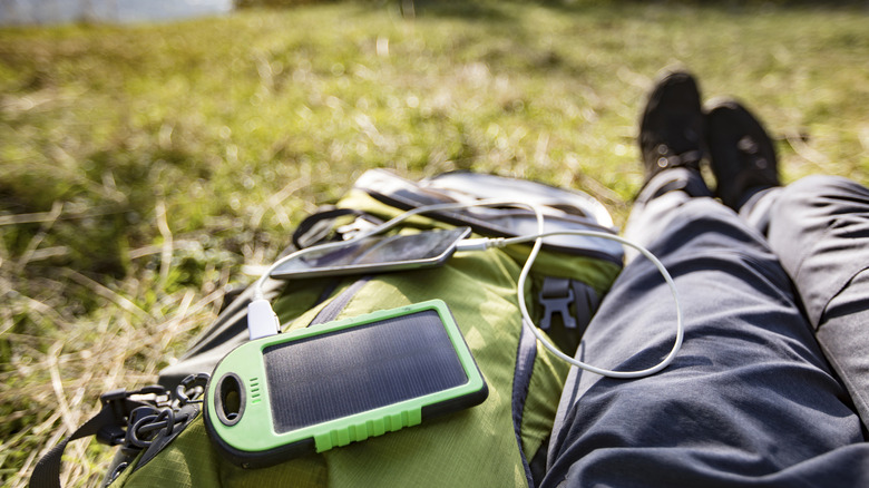 A portable solar-powered battery charging a phone while someone is outdoors
