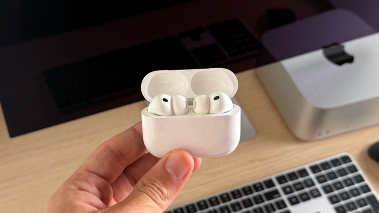 Apple's AirPods Pro 3 earbuds inside the charging case. Mac Studio and Studio Display are behind the earbuds.
