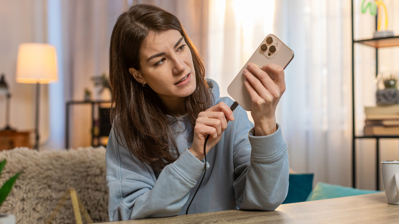 A woman in a blue sweatshirt looking at her phone as she plugs it in to a charging core