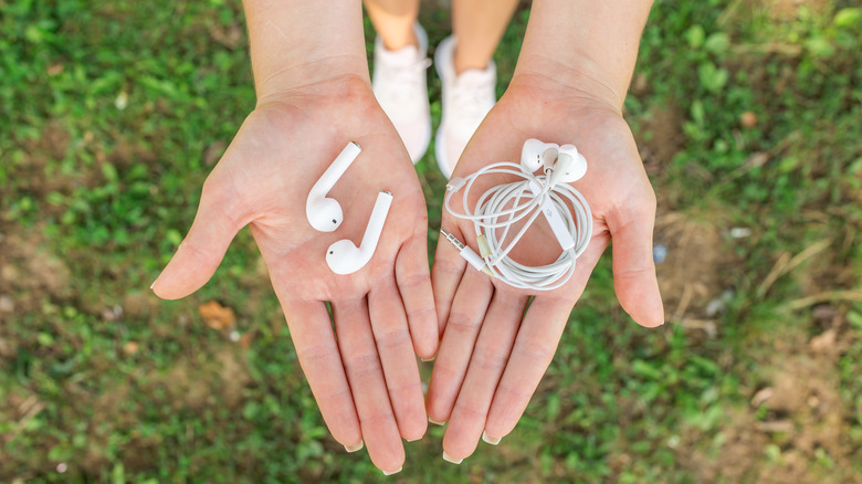 Hands holding wireless and wired earbuds side by side