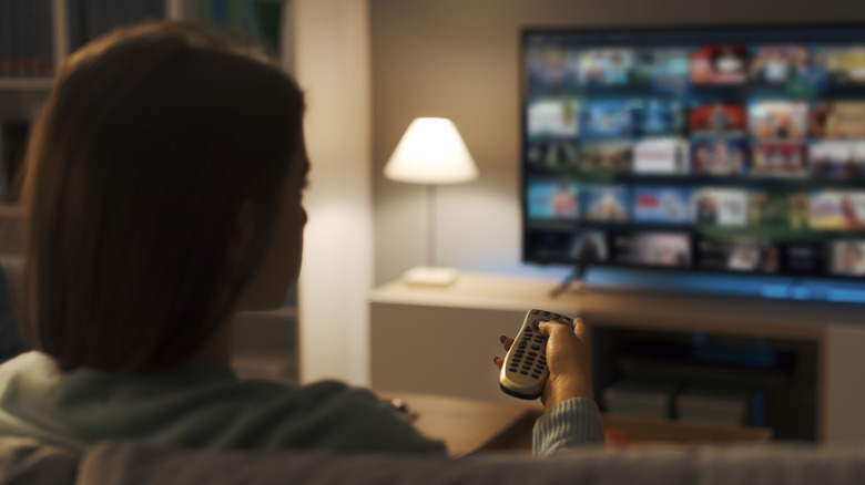Woman sitting on couch and pointing remote control at TV