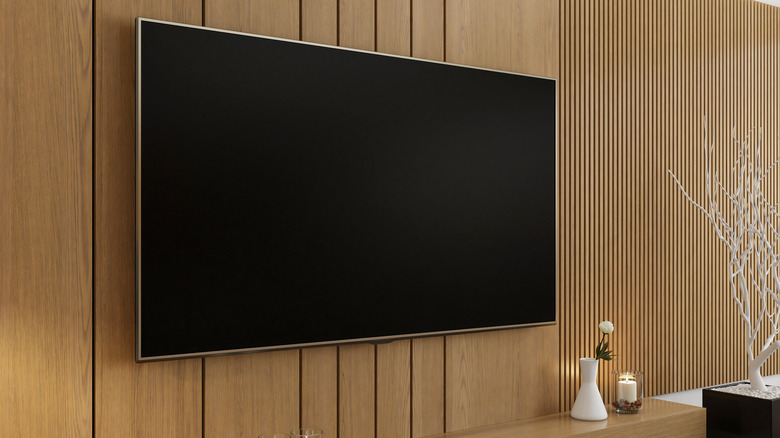 Large flat-screen, wireless TV mounted on wood paneling accompanied by candles on floating shelf below