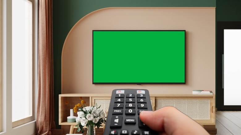 Person pointing remote control at wireless TV screen mounted on wall