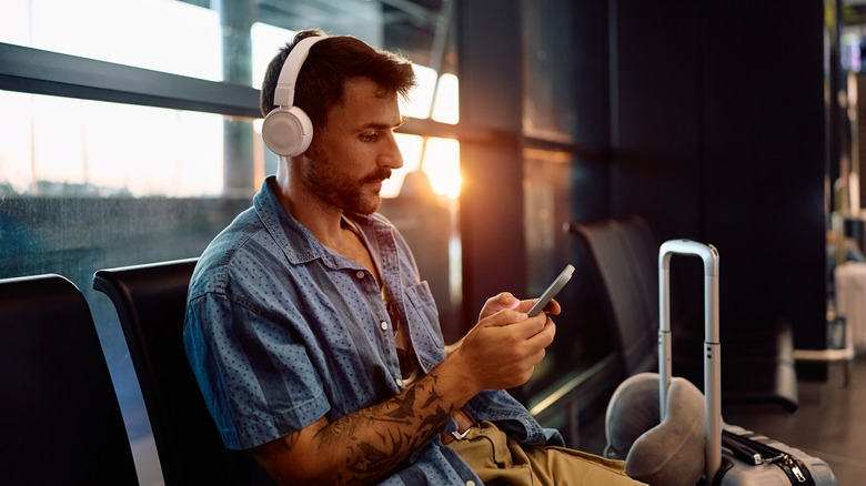 A man wearing headphones and using his phone at the airport.