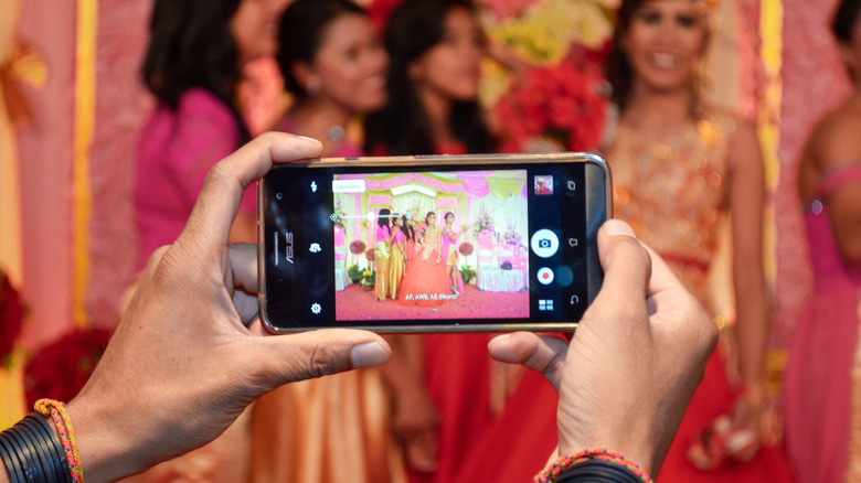 Hands holding Asus Zenfone, taking a group photo of women in formal attire