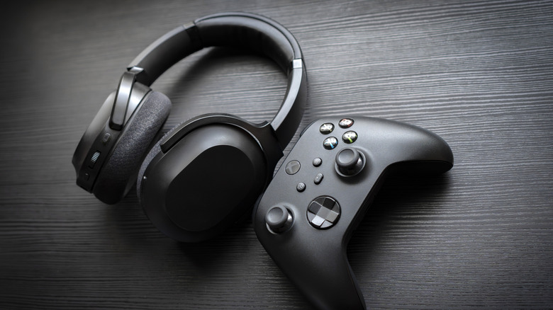 A black Microsoft Xbox controller sitting next to a pair of black over the ear headphones