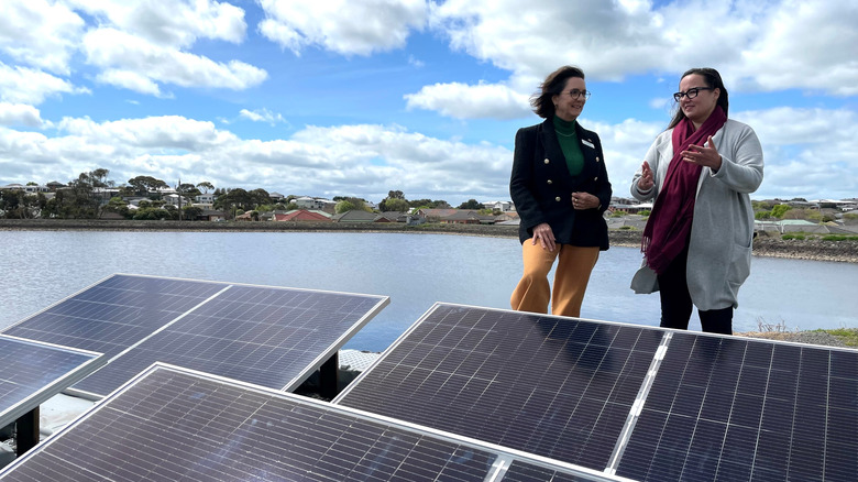 Two women stand behind a series of solar panels, which are being readied to be installed at Australia's largest floating solar plant on the Brierly Basin.
