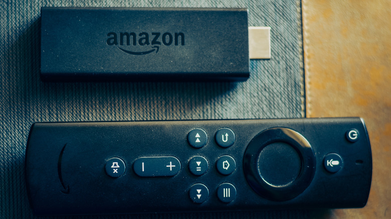 An older version of an Amazon Fire TV Stick streaming device lays next to its remote.