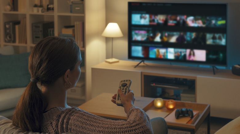 A person watching TV in a living room holding a remote control in their hand.