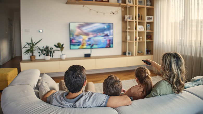A family sitting on a couch watching a wall-mounted TV.