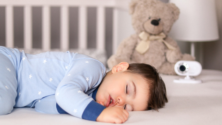 A baby sleeping with a camera and teddy bear in the background.