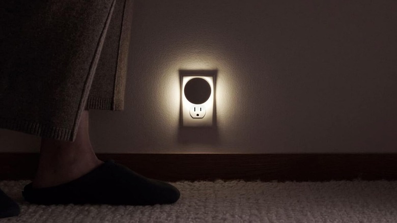 The Casper Sleep Glow night light plugged into an outlet, with a person walking in slippers nearby.