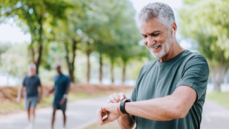 An older man on the street smiling while looking at his smartwatch.