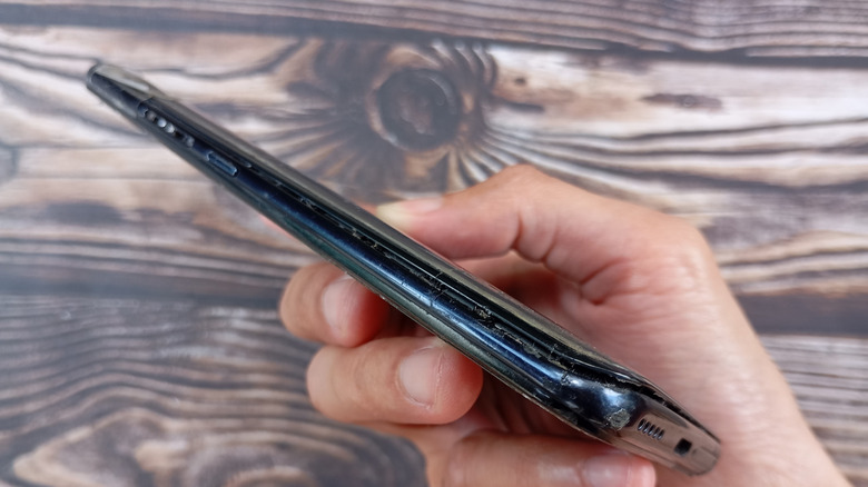Person holding a damaged smartphone with swollen battery