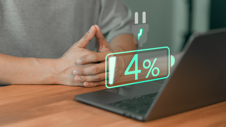 Graphic displaying 4% battery life with plug-in symbol above, person using laptop in background