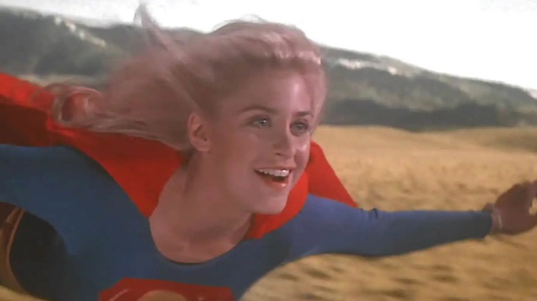 Helen Slater as Supergirl in the 1984 film of the same name. In this screenshot, Slater appears to be flying over a field with a mountain in the background, she has a big smile on her face.