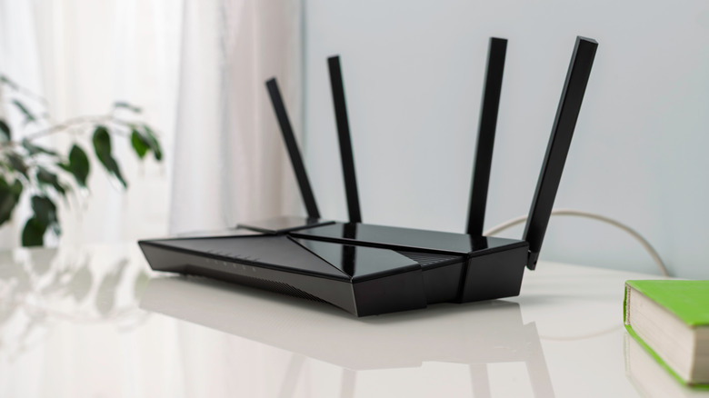 A router on a desk next to a plant and a book