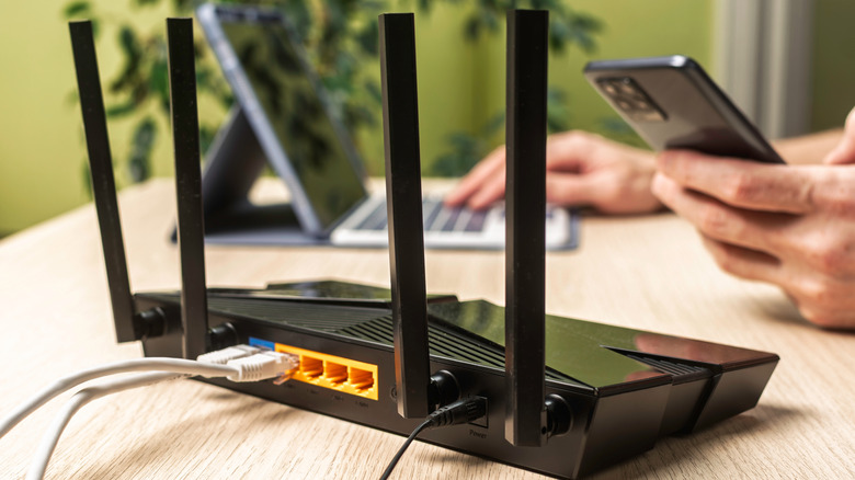 A router on a desk while a person works on a phone and a computer in the background