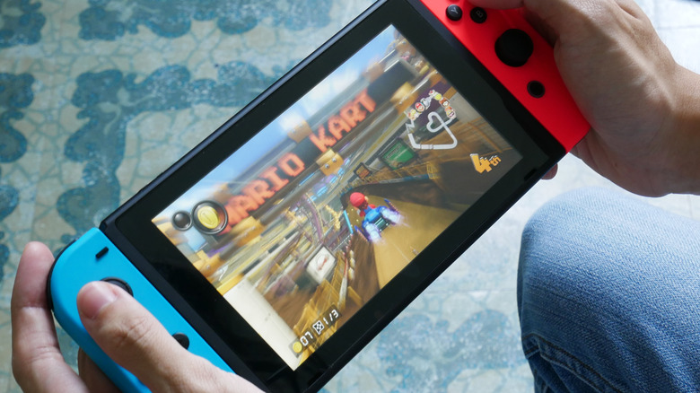 Someone holding the left Joy-Con, with a Nintendo Switch in the back ground