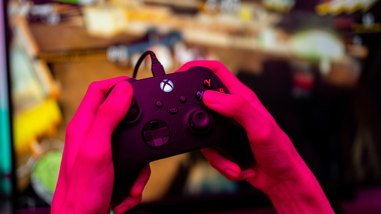 Someone holding a wired Xbox controller with red light in the foreground.