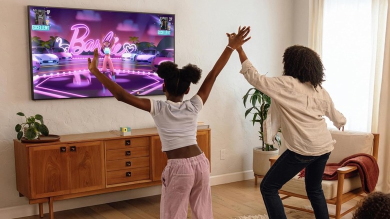 Mother and daughter playing Nex Playground console in the living room, Barbie game on screen.