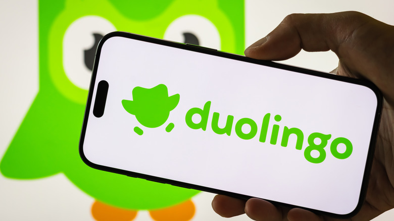 A person holds a smartphone displaying the Duolingo logo