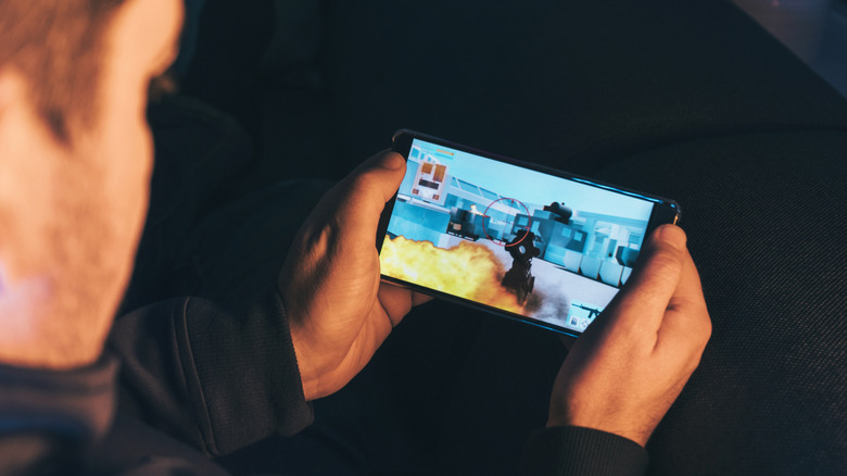 A person sitting down playing an action-shooter game on their phone