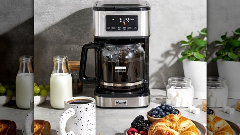 Coffee maker placed in a kitchen alongside milk, sugar cubes, and other food items