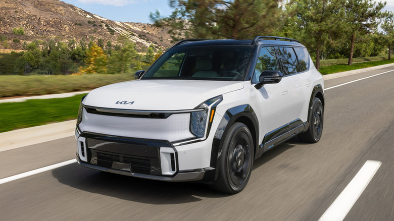 A white Kia EV9 driving on a road in the countryside