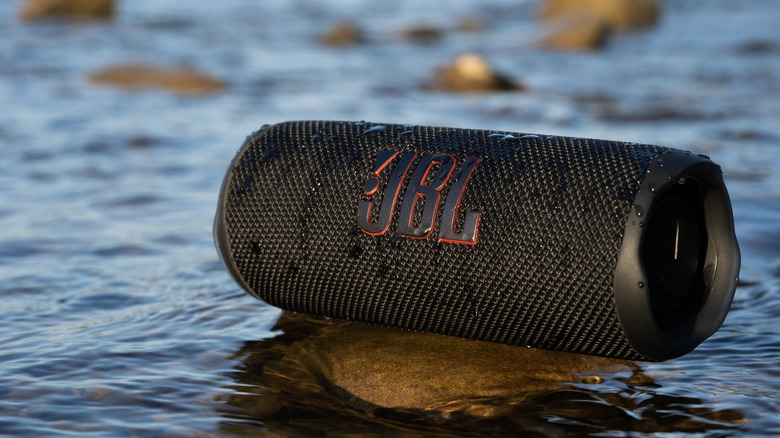 The JBL Flip 6 placed on top of a rock with water flowing around it. The speaker is also wet.