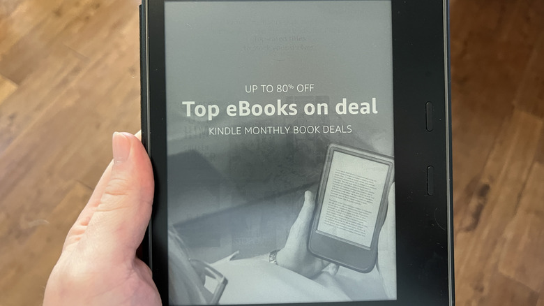 A hand holding an older Kindle eReader advertising a promotion with a wooden floor in the background