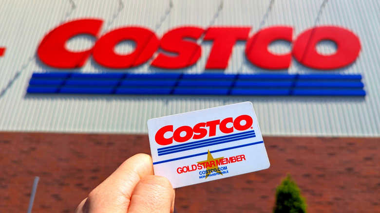 A person holding a Costco Gold Star Member card in front of a Costco logo.