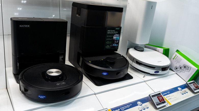 Three differently branded robot vacuums on the shelf of an electronics store.
