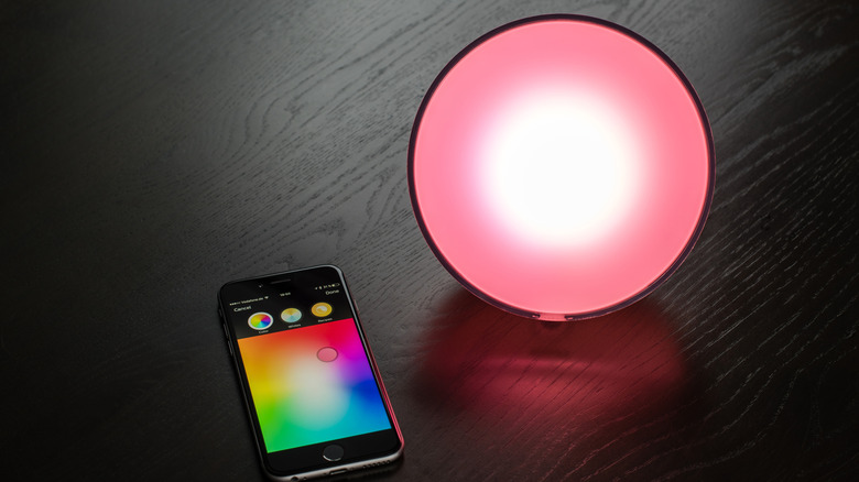 RGB smart lamp resting next to smartphone with customization screen showing.