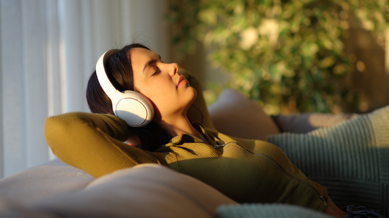 A woman wearing wireless headphones reclining on a rouch with her eyes closed.