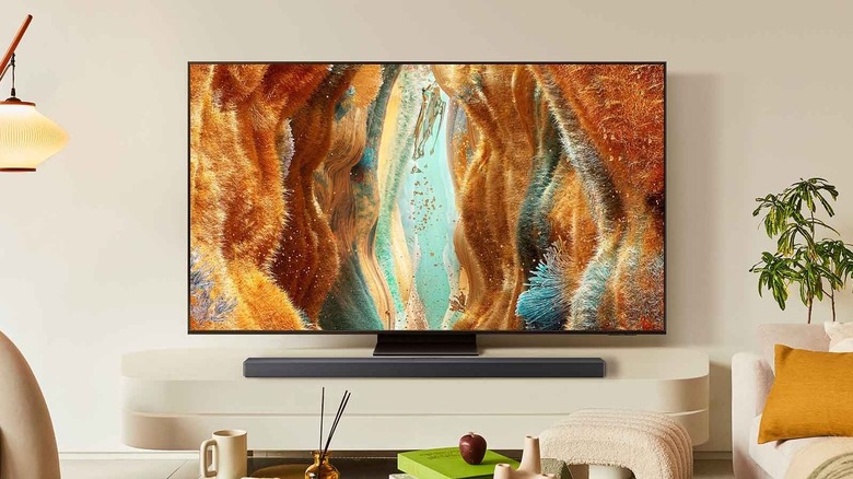 A Samsung QN70F Neo QLED placed on a TV unit in a living room, with a soundbar placed in front of it