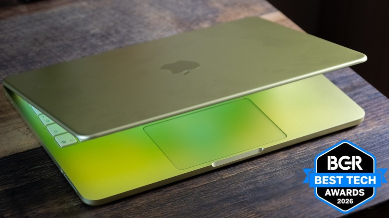 Yellow MacBook Neo on rough wood desk with lid partially open.