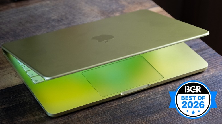 Yellow MacBook Neo on rough wood desk with lid partially open.